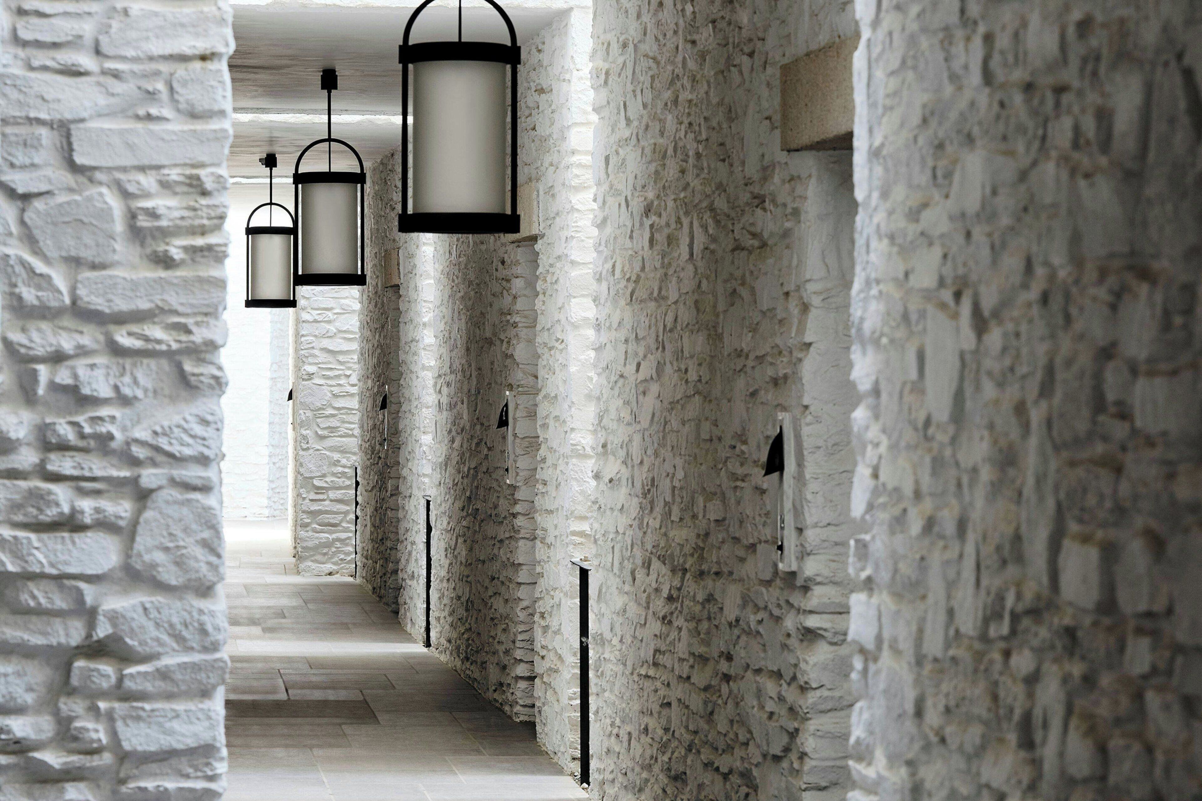 Un couloir aux murs de pierre, éclairé par des lanternes suspendues.