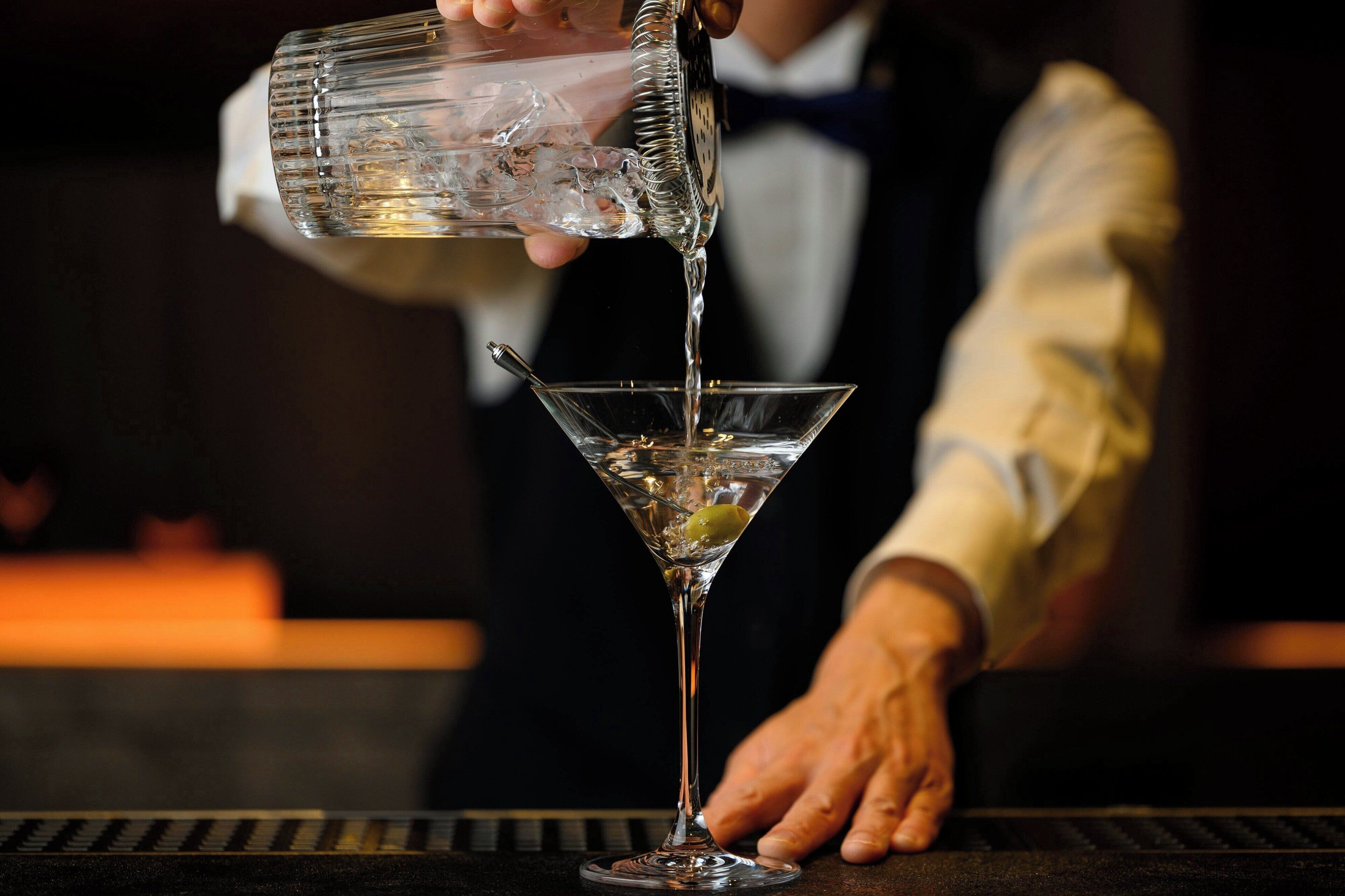 A bartender pouring a drink into a martini glass.