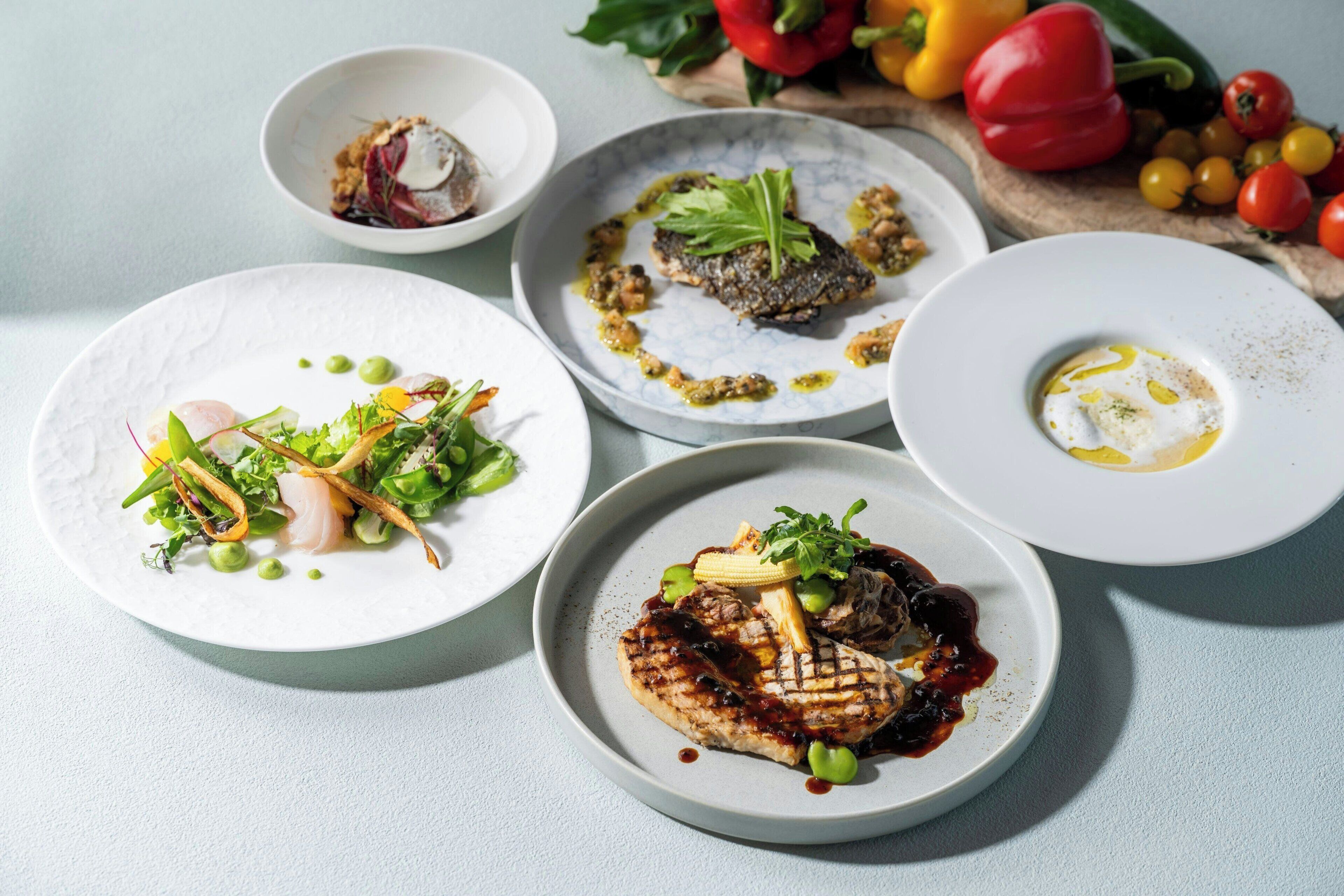 A table with various dishes, including grilled meat, vegetables, and a fish dish.