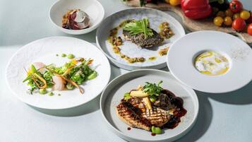 A table with various dishes, including grilled meat, vegetables, and a fish dish.