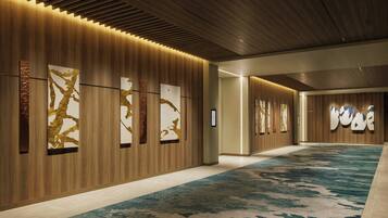 A modern hotel corridor with wooden panel walls, large abstract art pieces, and a patterned carpet.