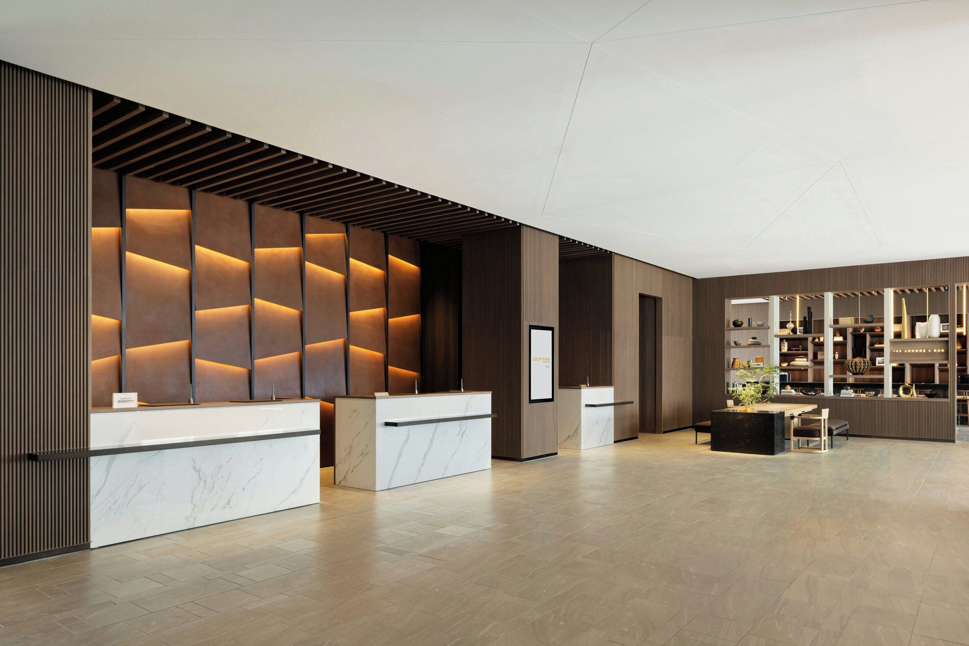 A modern reception area with a marble counter, wooden paneling, and a seating area with a plant.