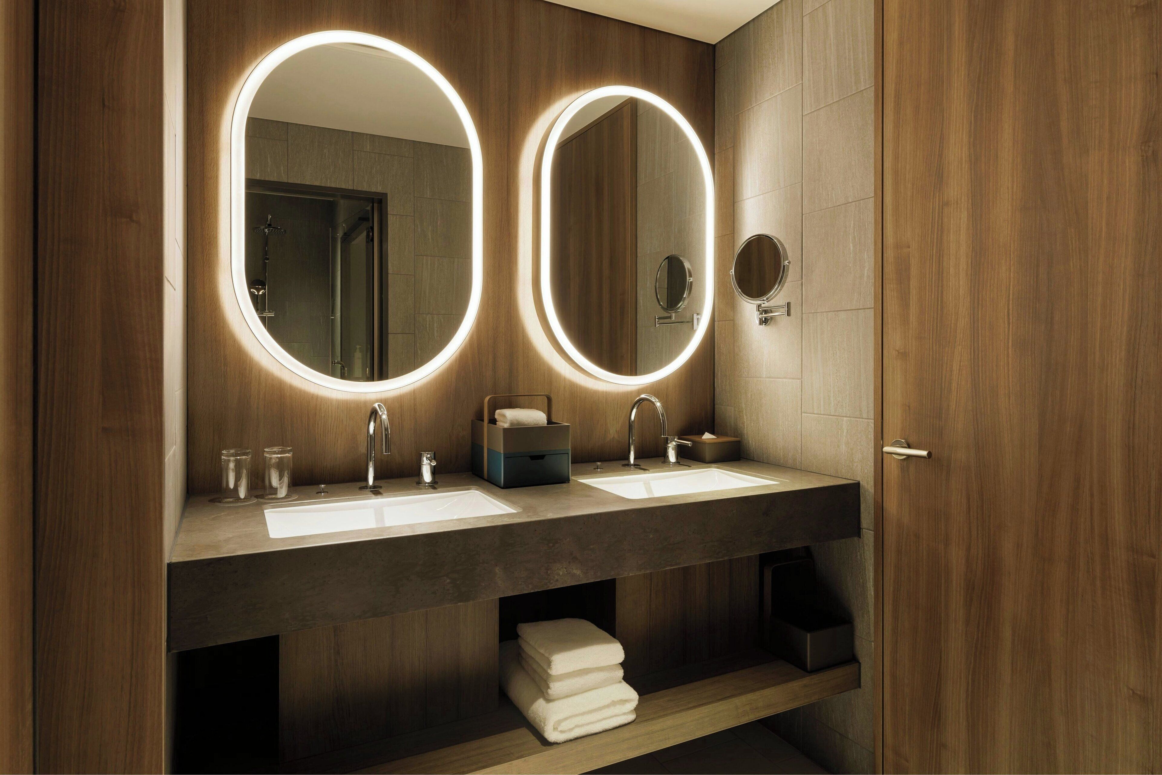 A modern bathroom with two sinks, illuminated mirrors, and wooden paneling.