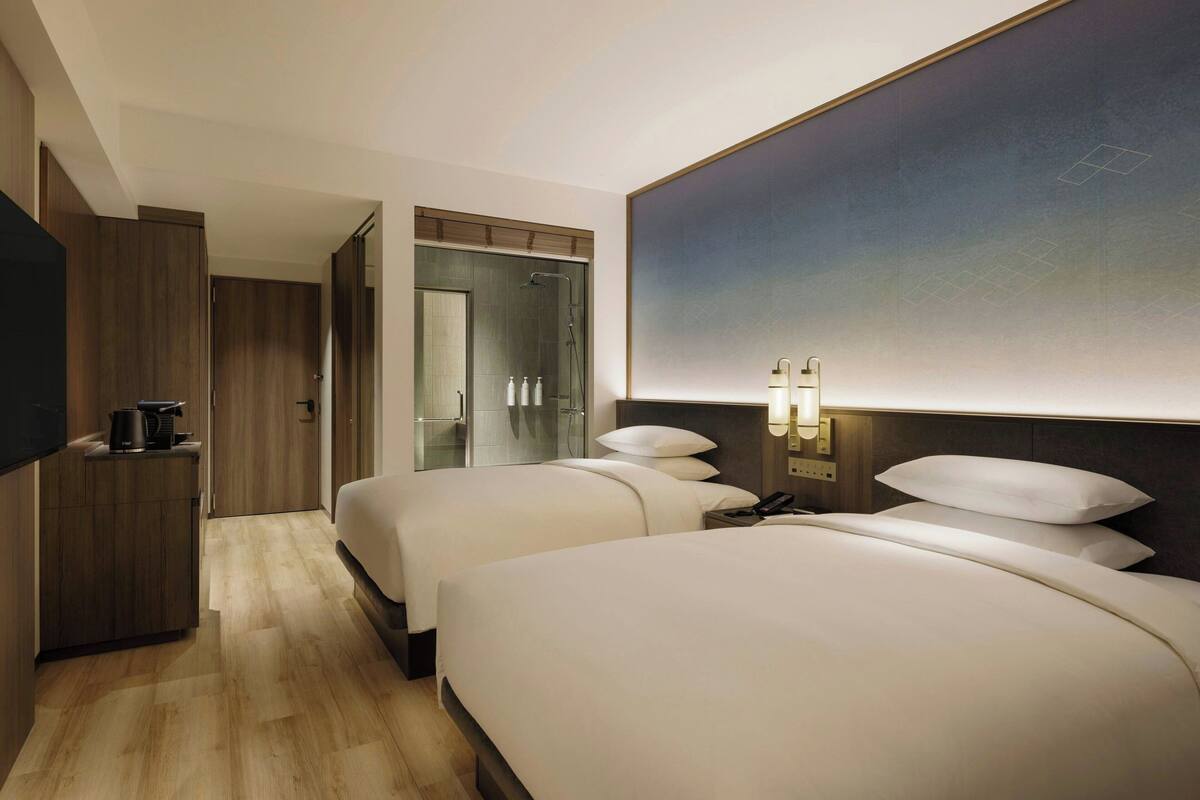 Ett hotellrum med två sängar, en garderob i trä, en minibar och en duschhörna.