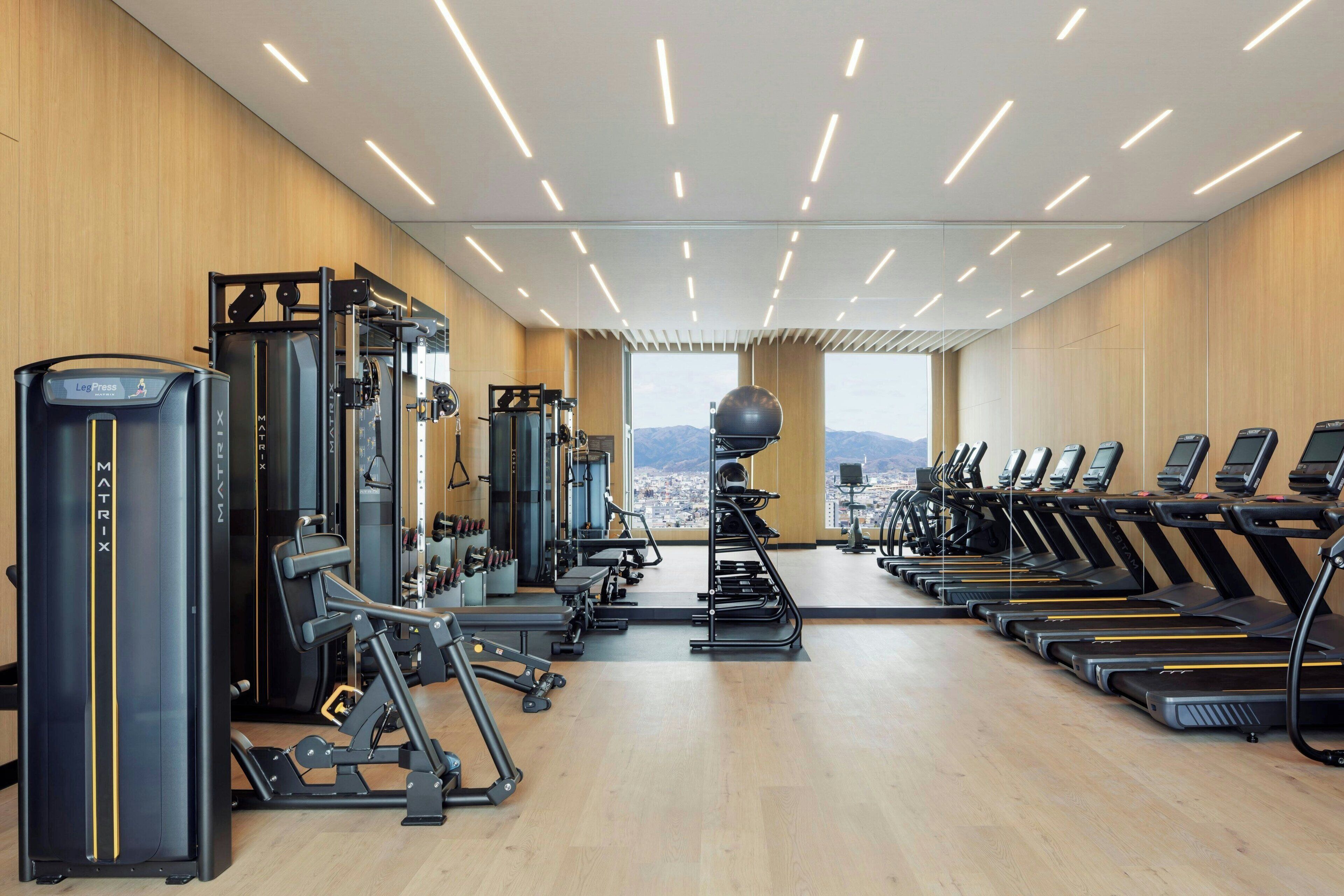 A gym with cardio equipment, weight machines, and a view of the city.