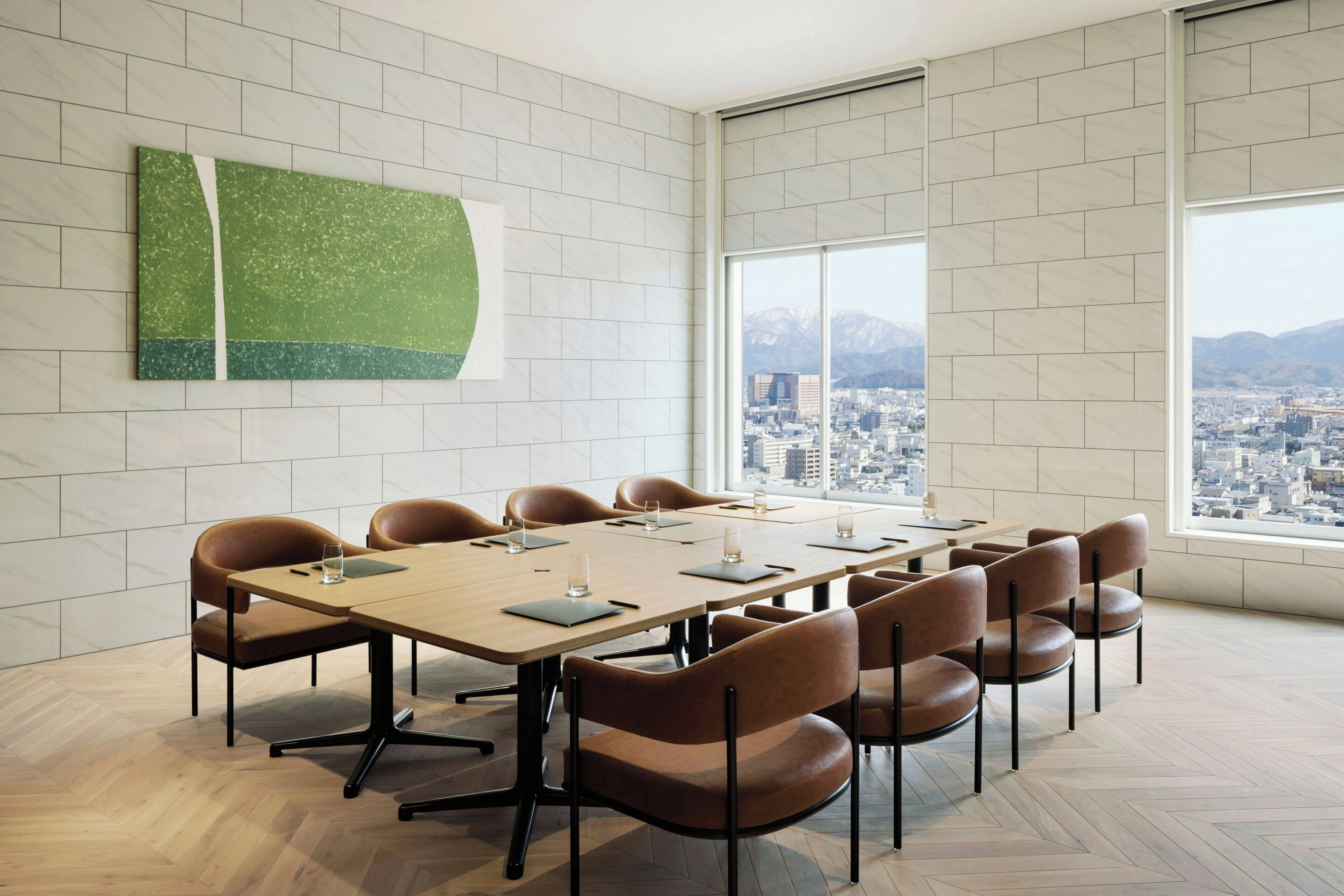 A conference room with a large table, brown chairs, and a city view through large windows.