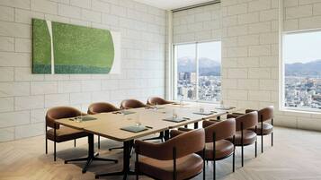 A conference room with a large table, brown chairs, and a city view through large windows.