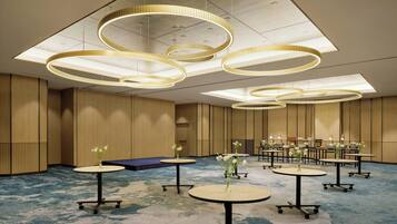 Une chambre d’hôtel moderne avec des luminaires circulaires au plafond, des tables rondes ornées de vases de fleurs et une moquette bleue.