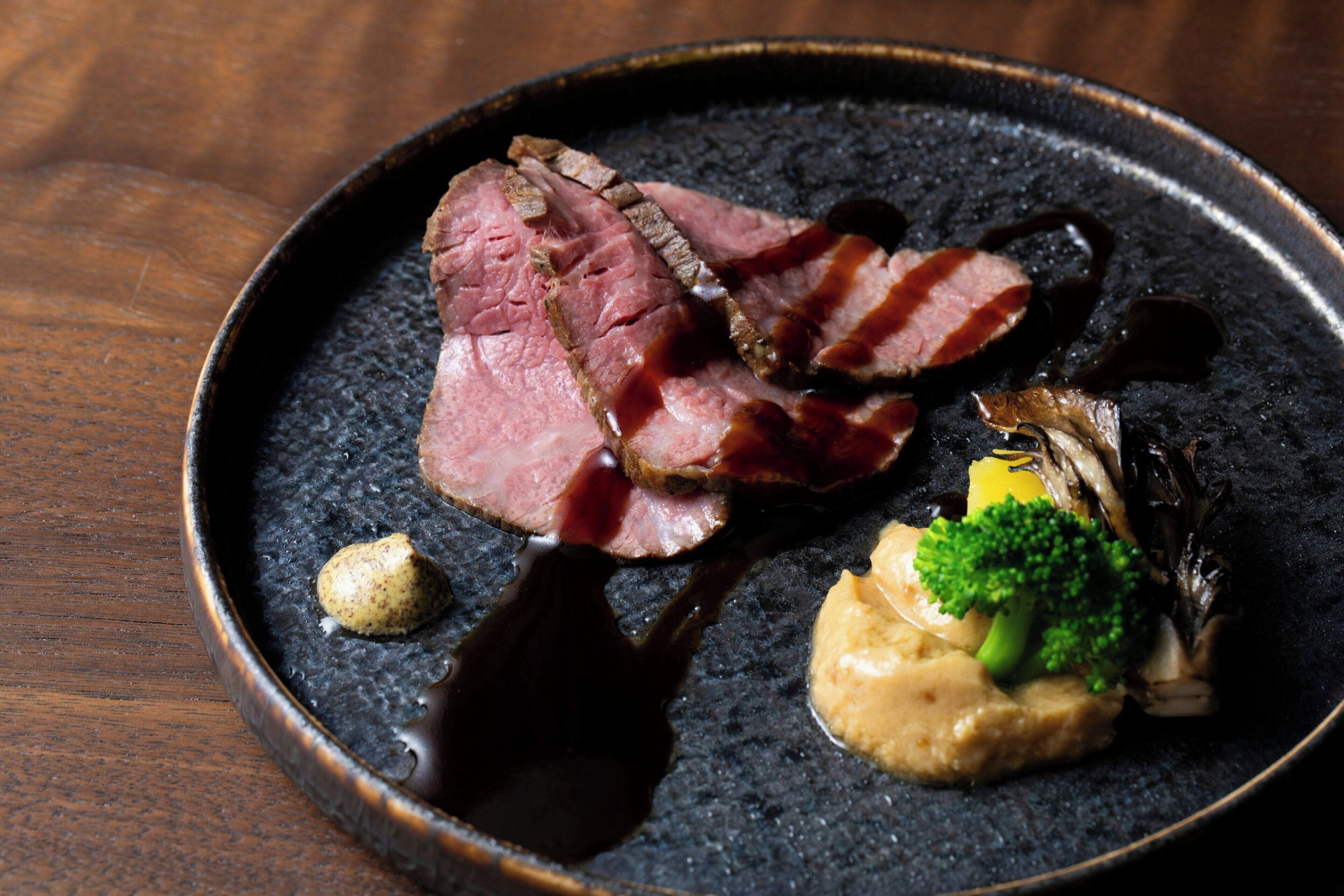 A plate of food with slices of meat, a piece of bacon, and some vegetables.