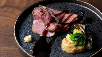A plate of food with slices of meat, a piece of bacon, and some vegetables.