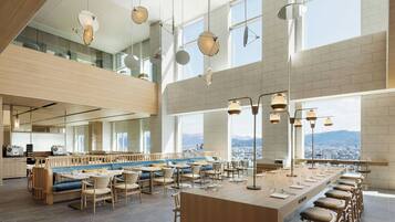 Een modern restaurant met hoge plafonds, grote ramen en een lange gedeelde eetruimte.