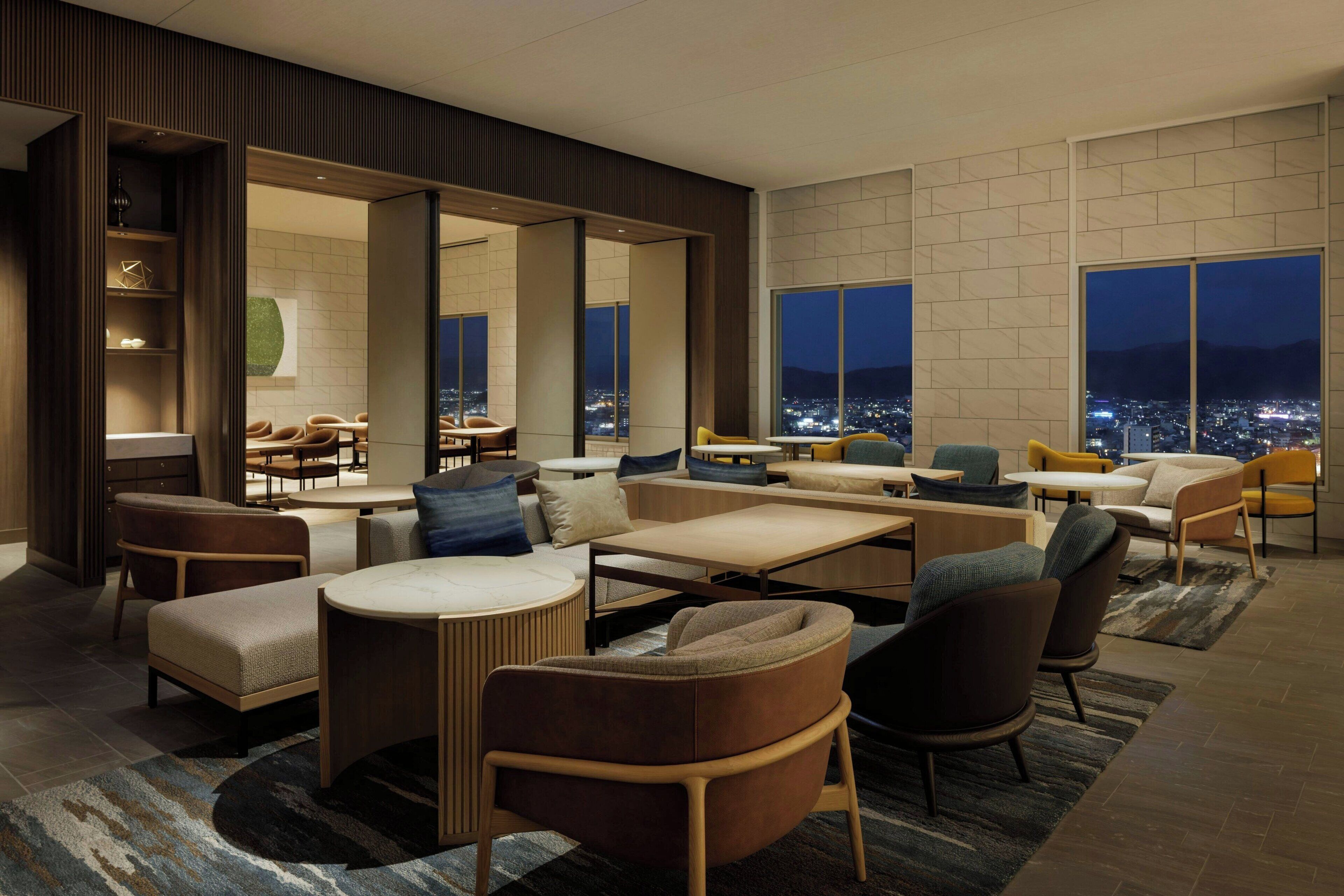 A modern hotel lobby with a seating area, large windows, and a city view.