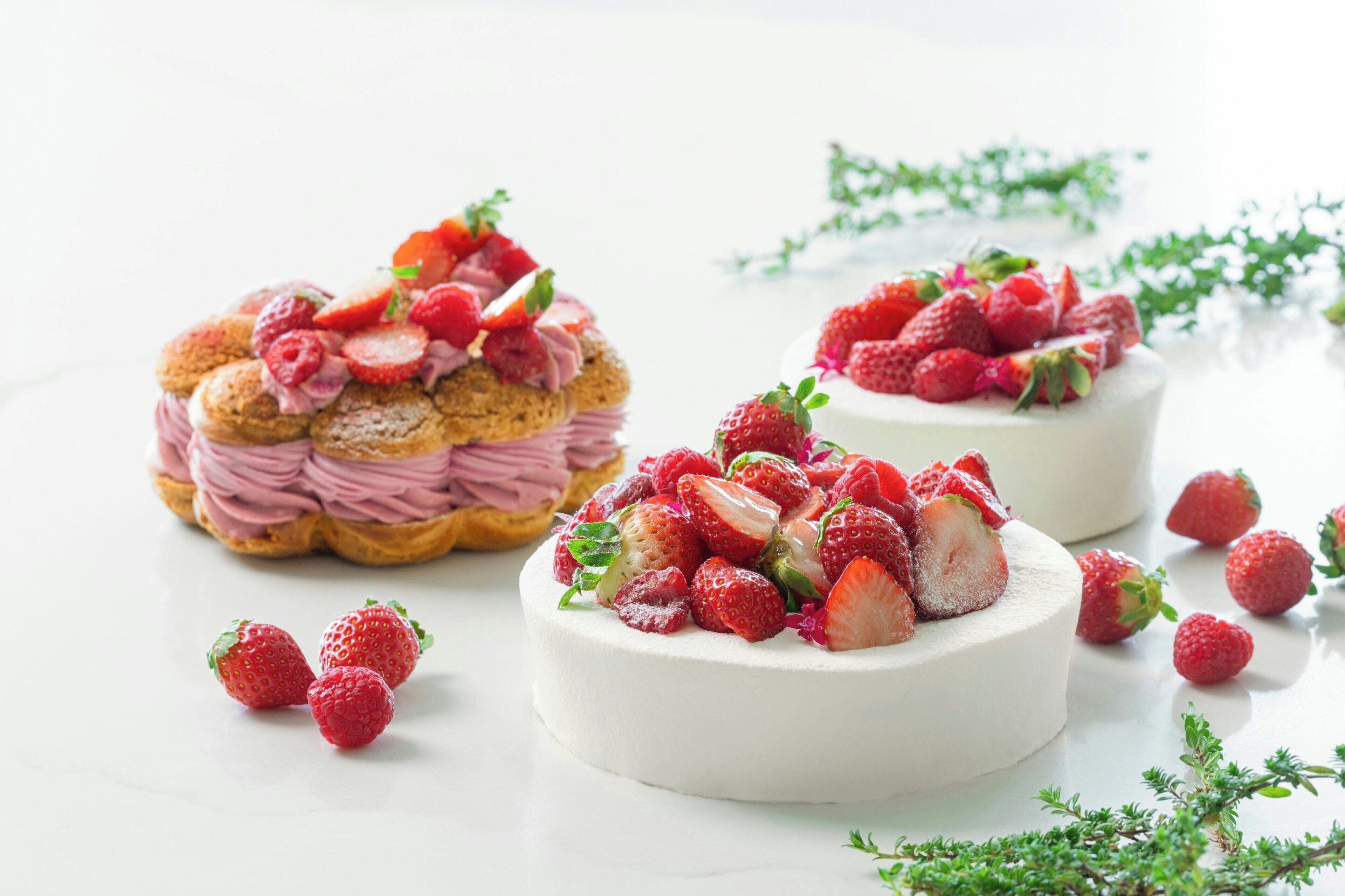 Two round desserts topped with strawberries and cream, surrounded by scattered strawberries on a white surface.