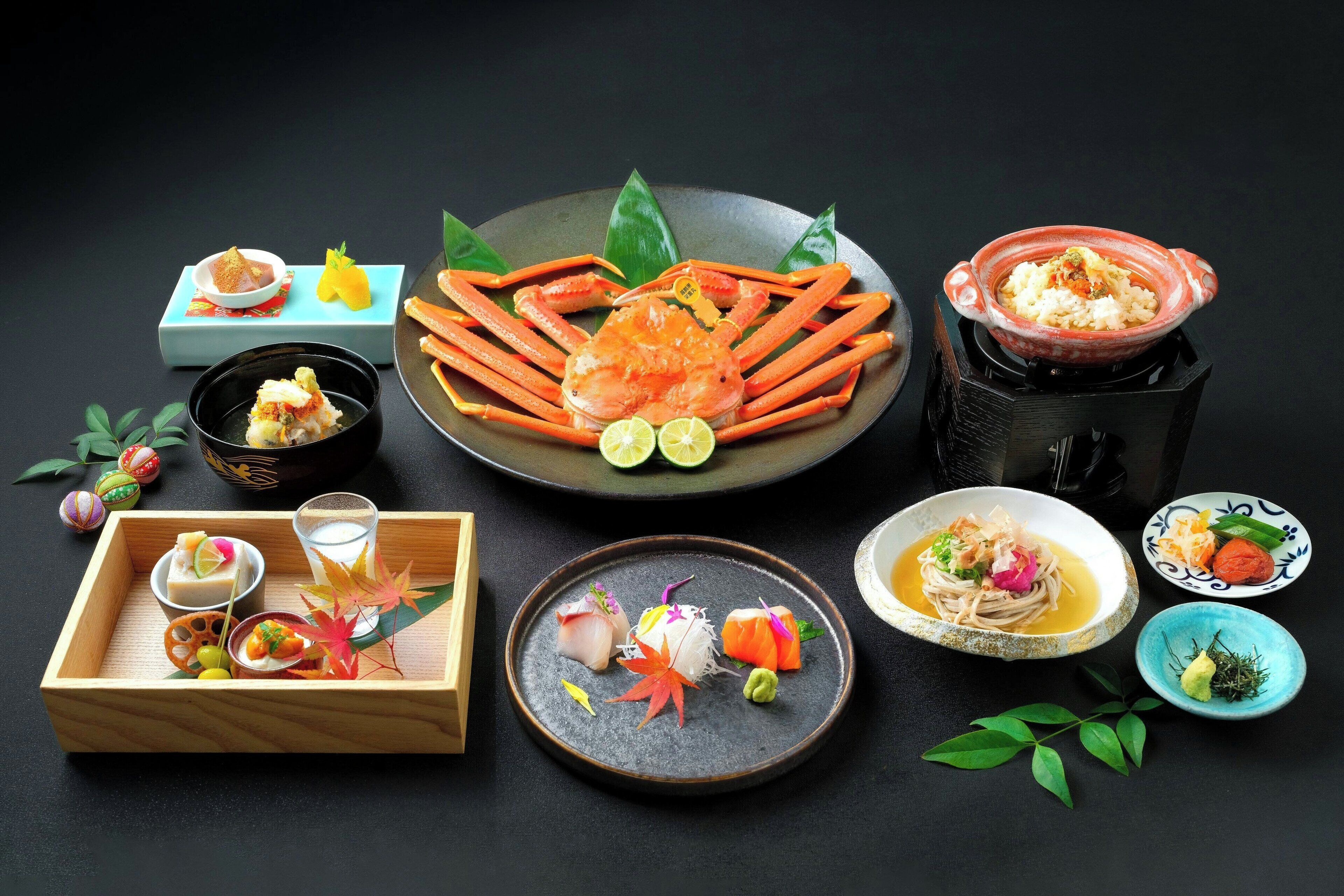 A variety of Japanese dishes including sushi, sashimi, and a crab dish, arranged on a dark table.
