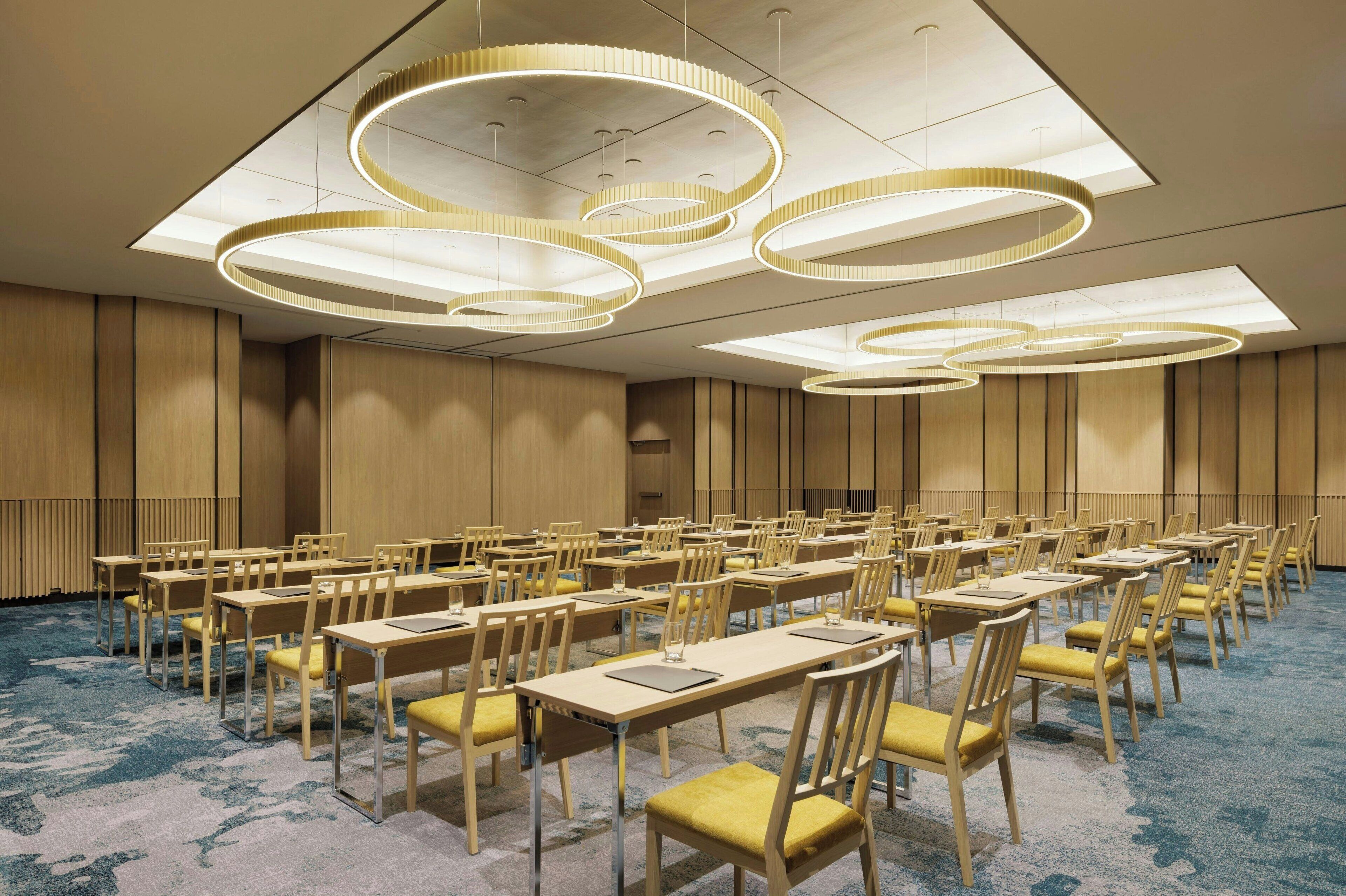 A conference room with multiple tables and chairs, large circular ceiling lights, and a patterned carpet.