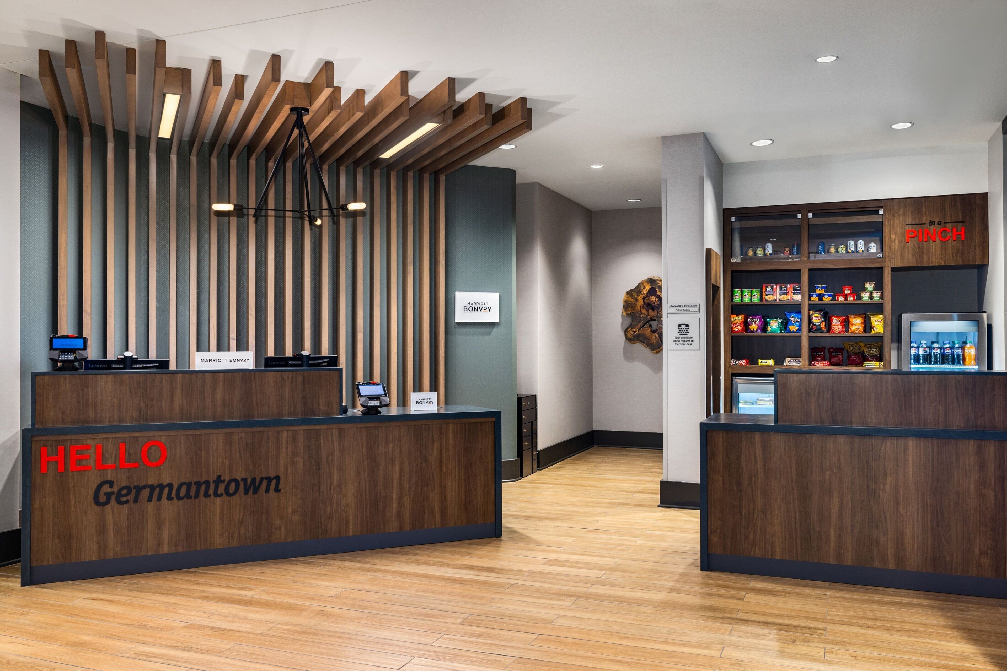 A hotel reception area with a wooden reception desk, a digital screen, and a minibar.