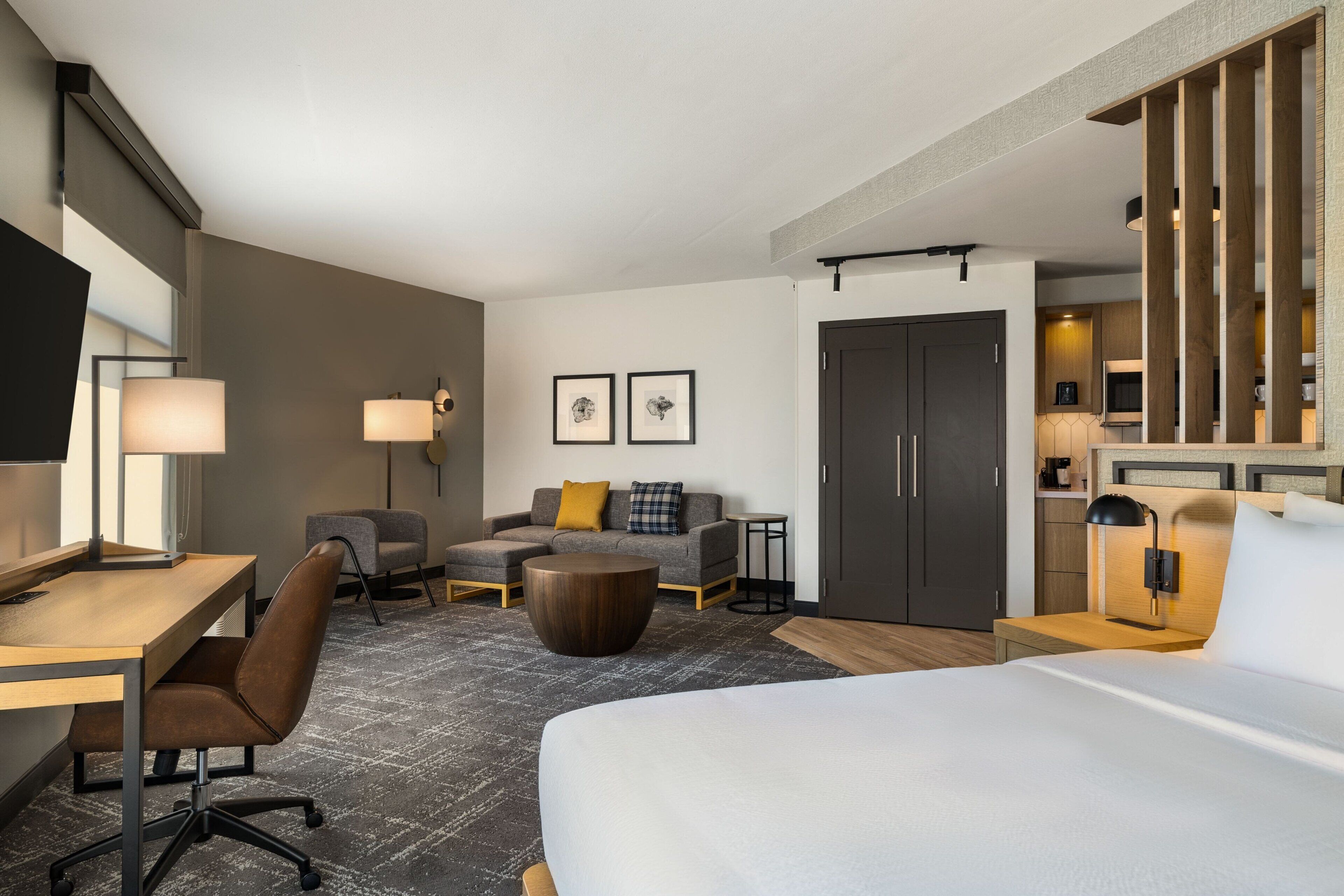 Una habitación de hotel moderna con una cama grande, un escritorio, un sofá, una mesa de centro y un área de comedor separada.