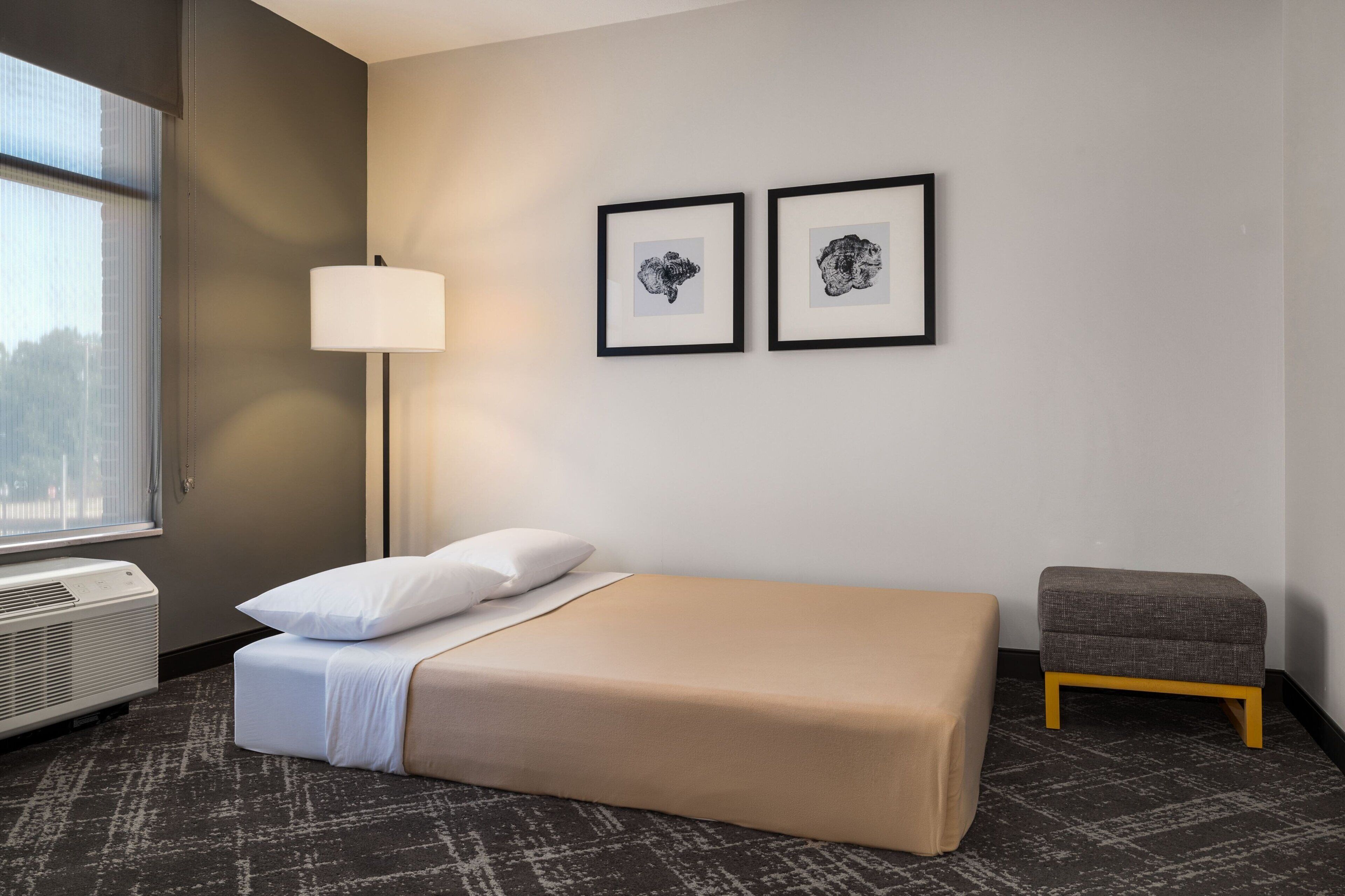 Una camera d'albergo con un letto, una lampada da comodino, un piccolo tavolo e due quadri appesi al muro.