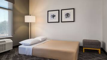 Una camera d'albergo con un letto, una lampada da comodino, un piccolo tavolo e due quadri appesi al muro.
