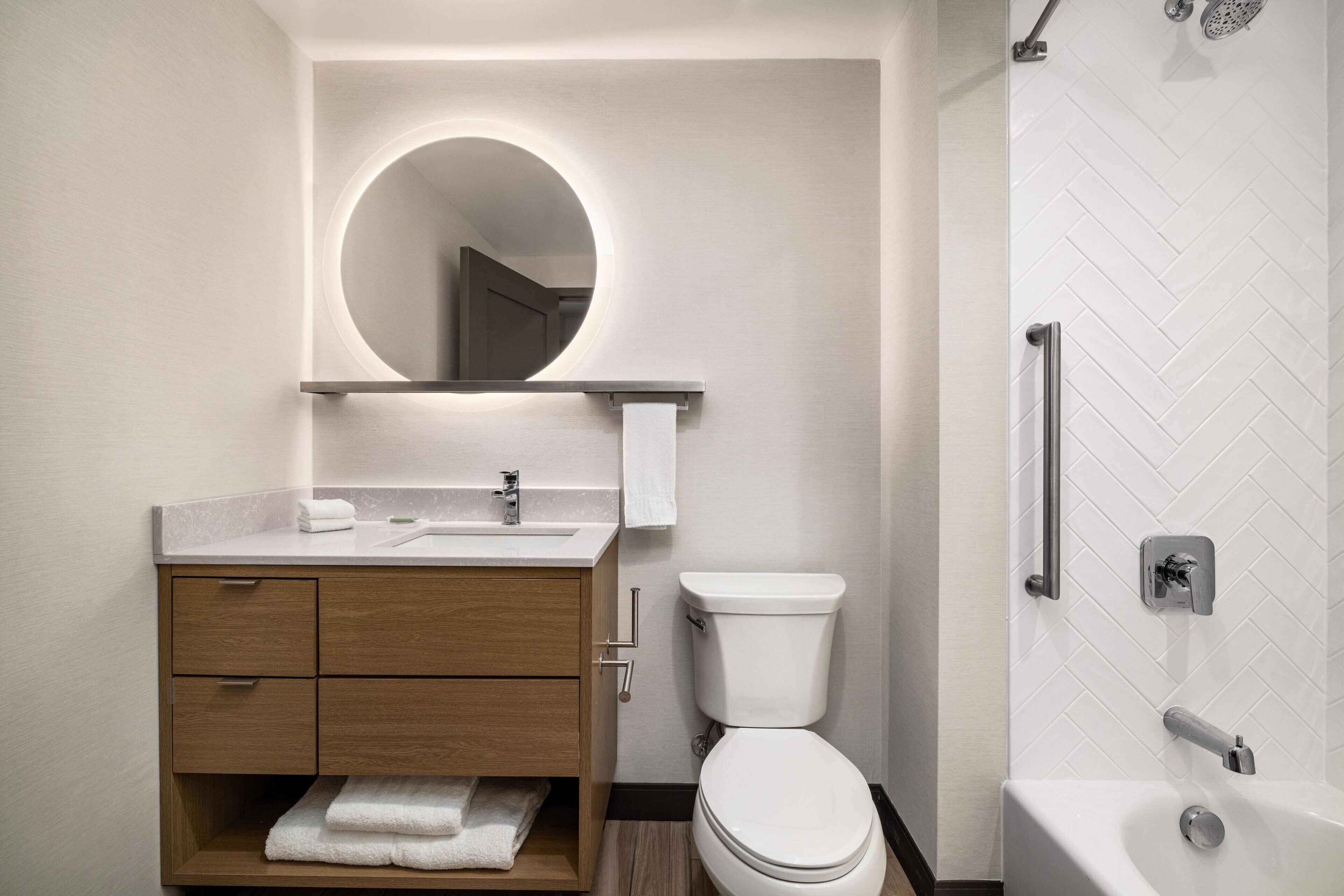 A modern bathroom with a wooden vanity, a round mirror, a toilet, and a shower area.
