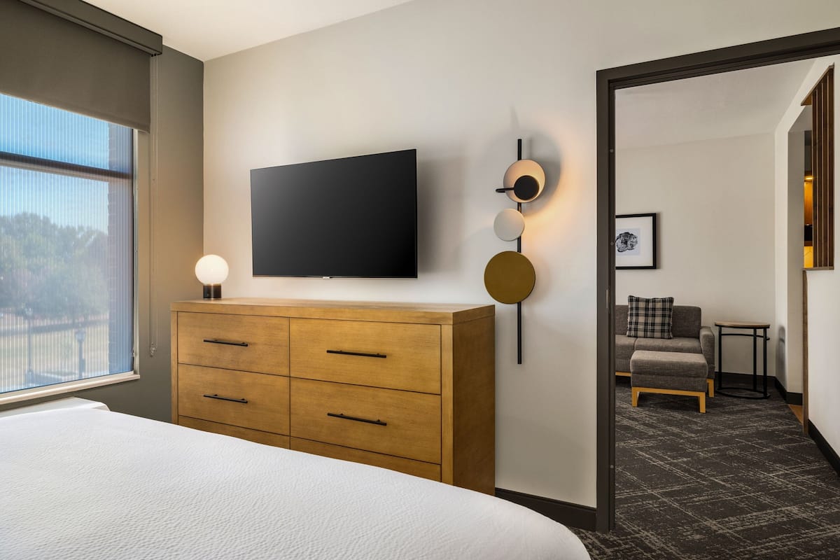 Habitación de hotel con una cama grande, un aparador de madera, un televisor de pantalla plana en la pared y una pequeña zona de estar con un sofá y una mesa.