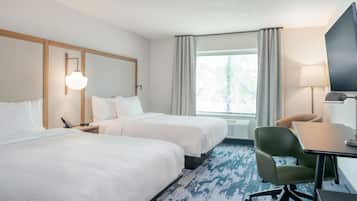 Habitación de hotel con dos camas, un escritorio, una silla, un televisor y una ventana con cortinas.