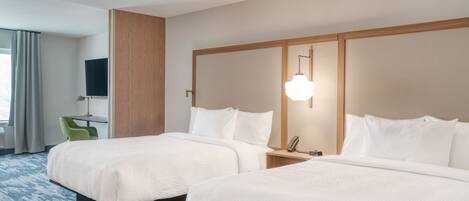 A hotel room with two beds, a desk, a chair, a TV, and a mirror.