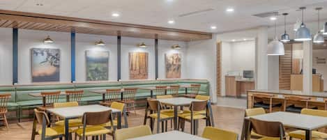 A modern restaurant with green booths, yellow chairs, and white tables.