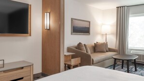 Habitación de hotel con cama, sofá, escritorio, televisor, lámpara y ventana con cortinas.