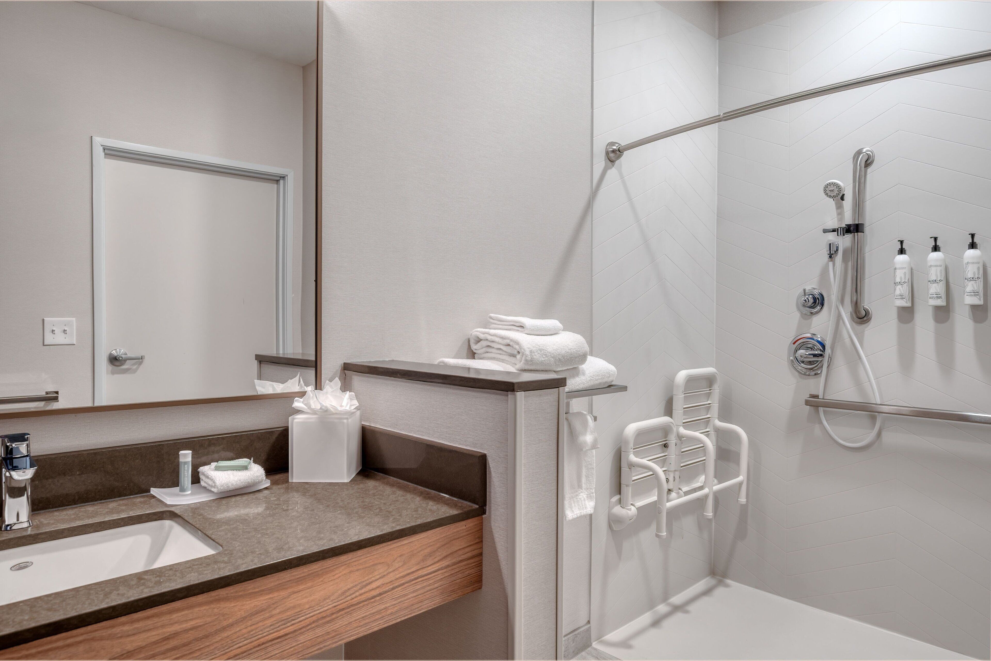 A modern bathroom with a sink, mirror, towel rack, shower, and toiletries.