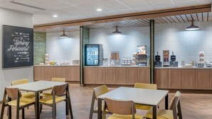 Una cocina moderna con armarios de madera, un refrigerador y una estación de café. Se observan dos mesas con sillas al frente.