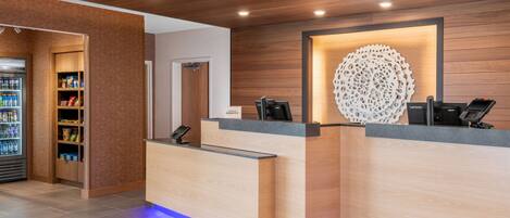 A reception desk with a wooden finish, a decorative wall piece, and a beverage refrigerator.