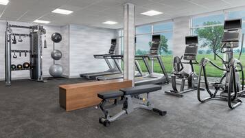 Una palestra con tapis roulant, ellittiche, una panca e attrezzature per sollevamento pesi.