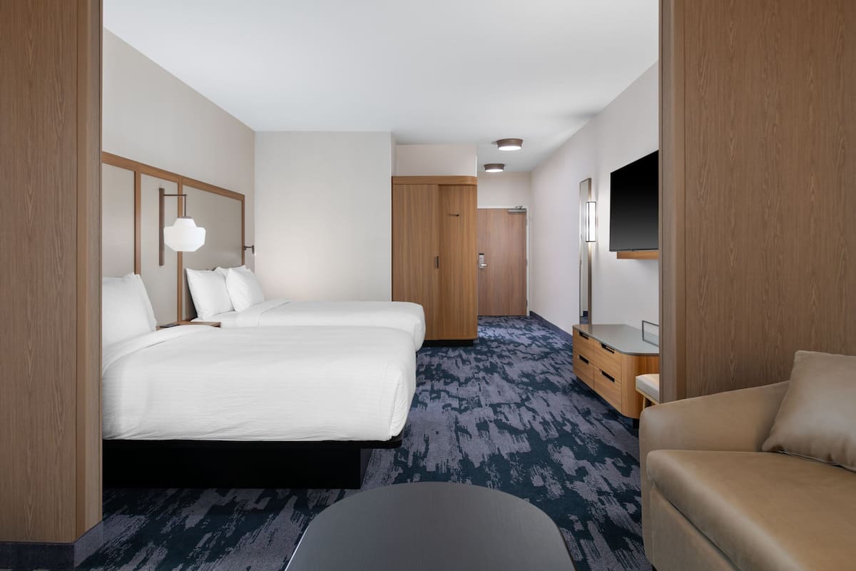A hotel room with two beds, a sofa, a TV, a desk, and a wardrobe.