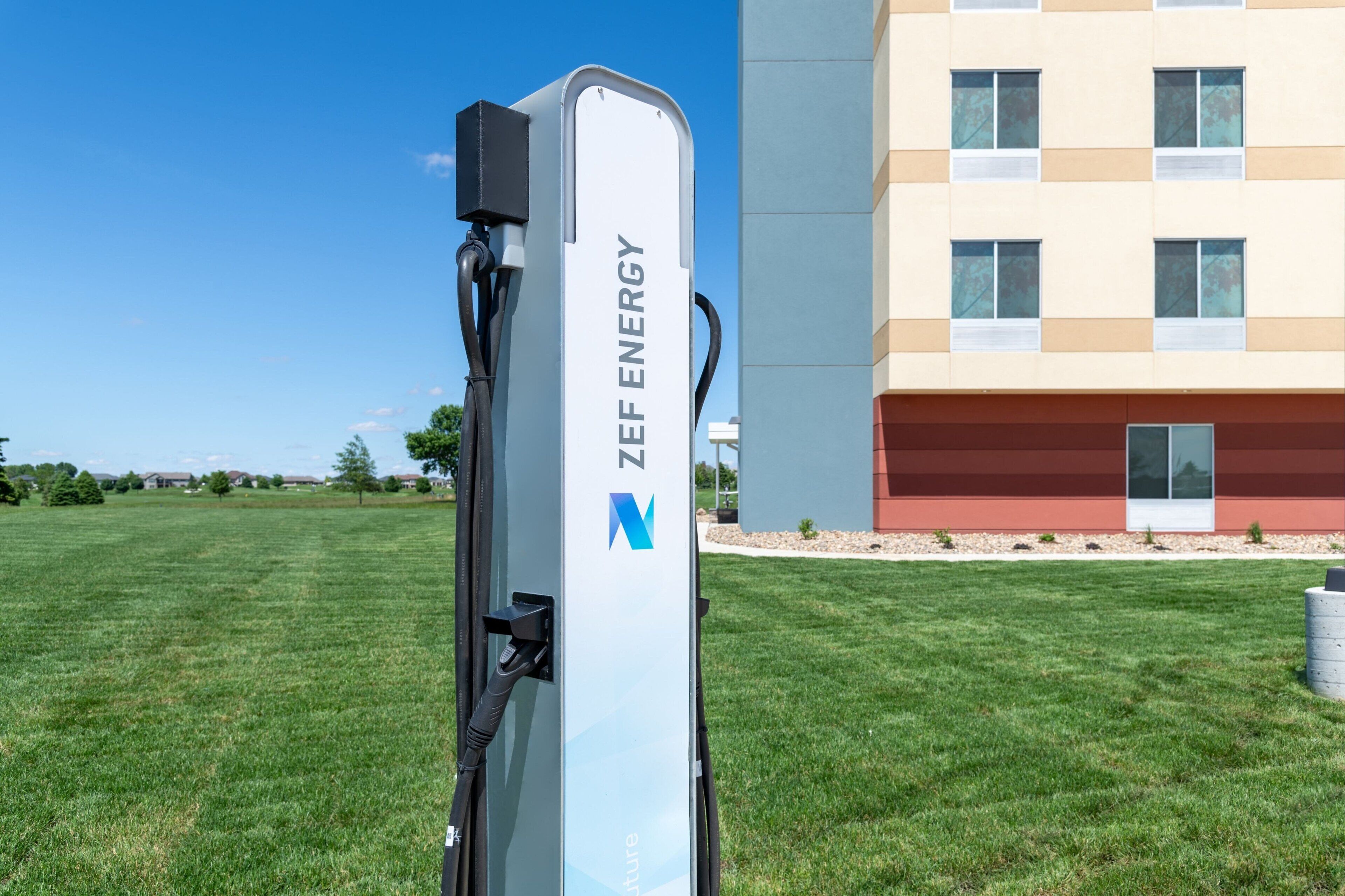 A ZEF ENERGY electric vehicle charging station in a grassy area with a modern building in the background.