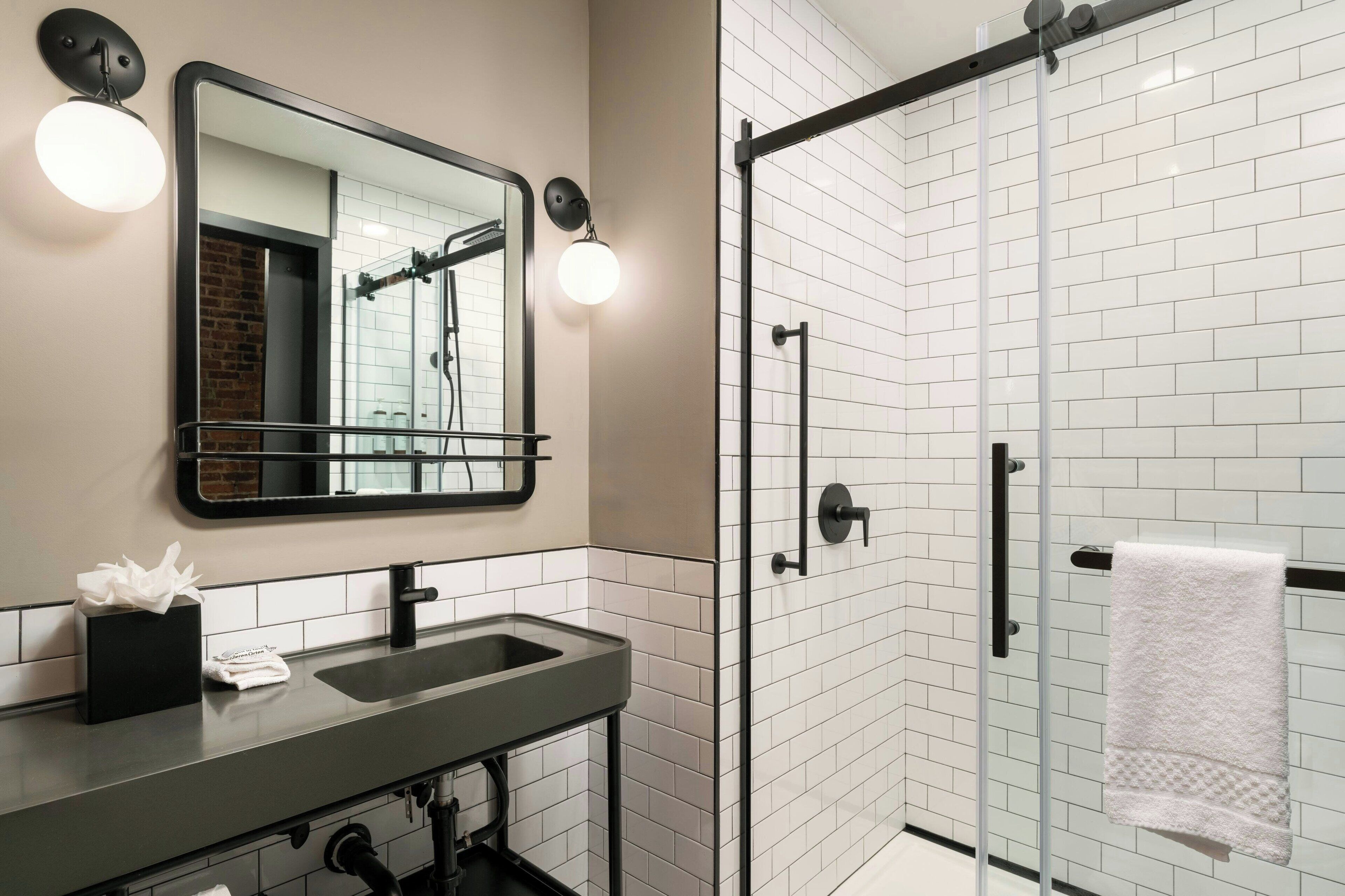 A modern bathroom with a large mirror, a sink, and a glass-enclosed shower.