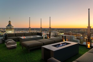 A rooftop lounge with a city view, including a prominent dome building, at sunset.