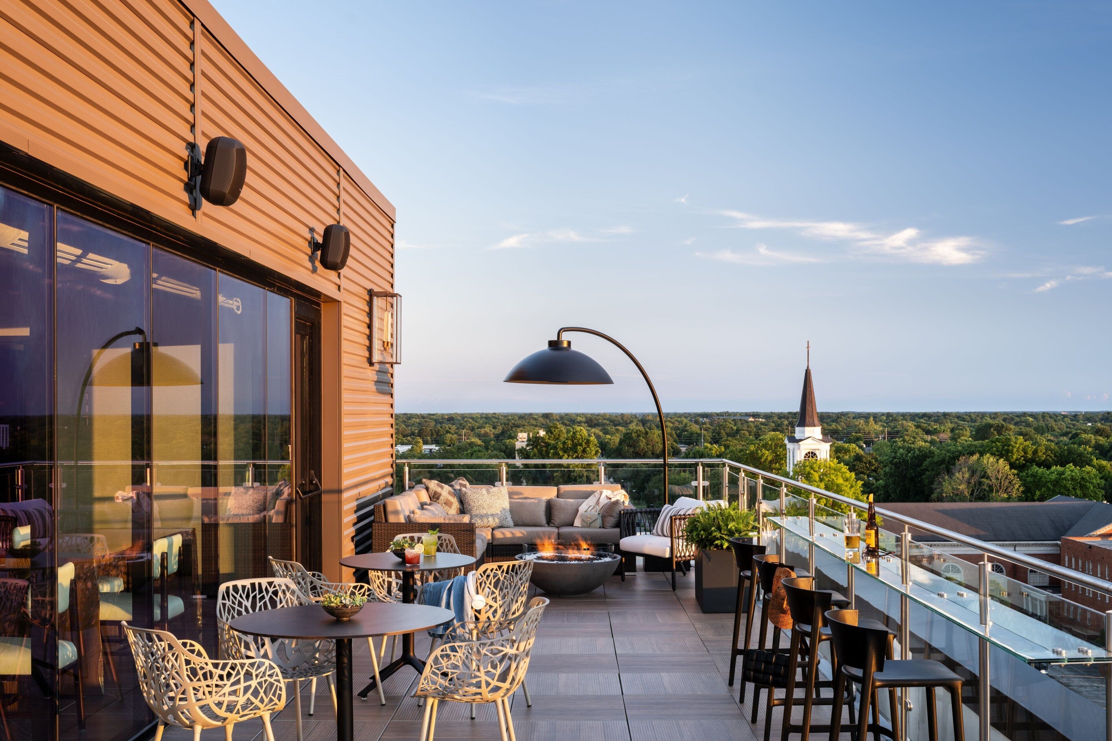 A rooftop terrace with outdoor seating, a fire pit, and a view of a church steeple.
