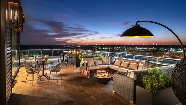 Une terrasse sur le toit avec un foyer, des sièges extérieurs et une vue sur la ville au crépuscule.
