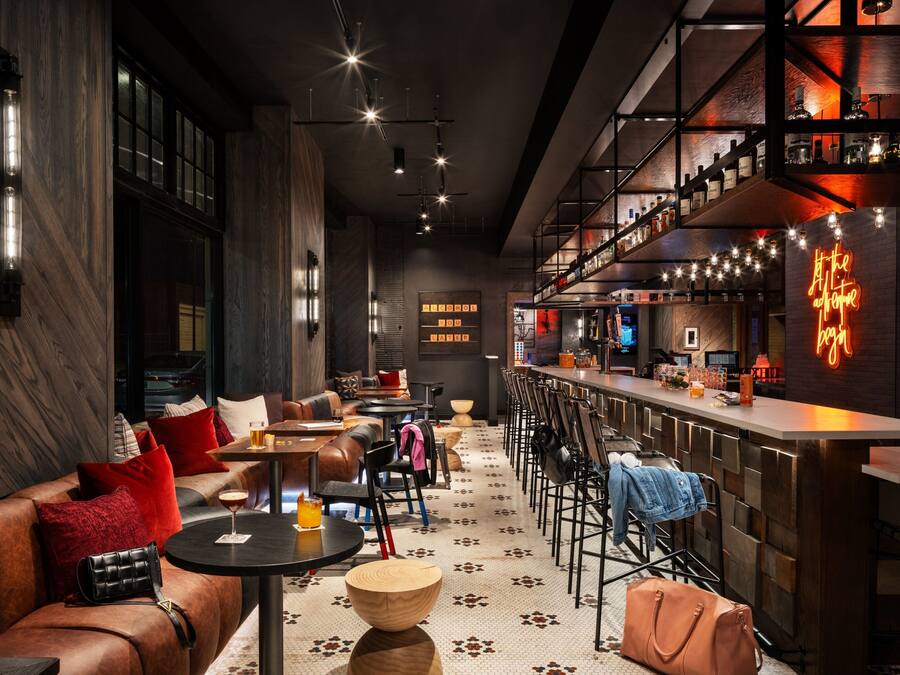 A modern bar area with leather seating, wooden tables, and a neon sign.