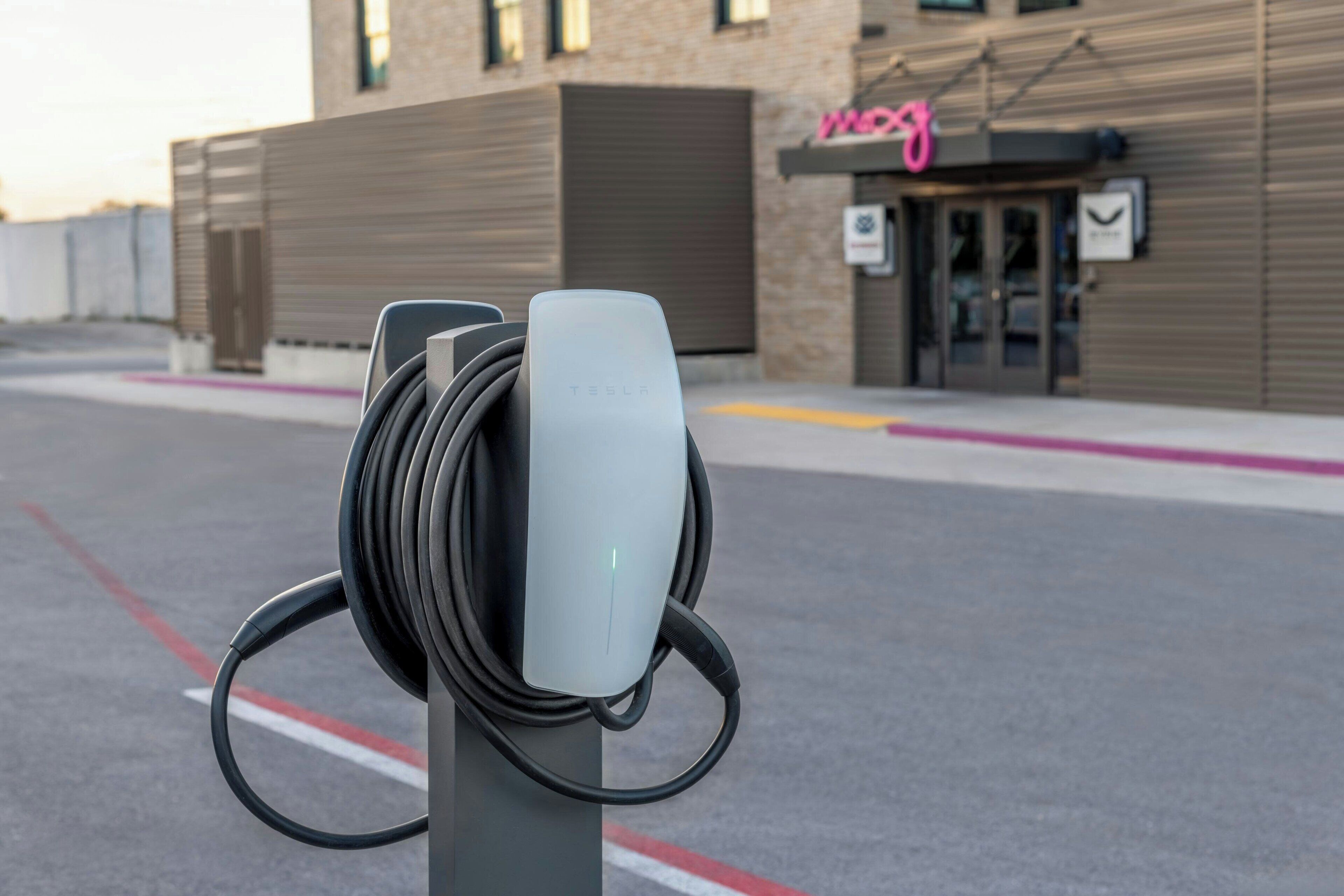 Una stazione di ricarica Tesla in un contesto urbano, con un edificio sullo sfondo.