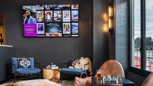 Un espace de détente moderne doté d’une grande fenêtre, d’un téléviseur fixé au mur diffusant différents contenus et d’un luminaire au plafond au design original.