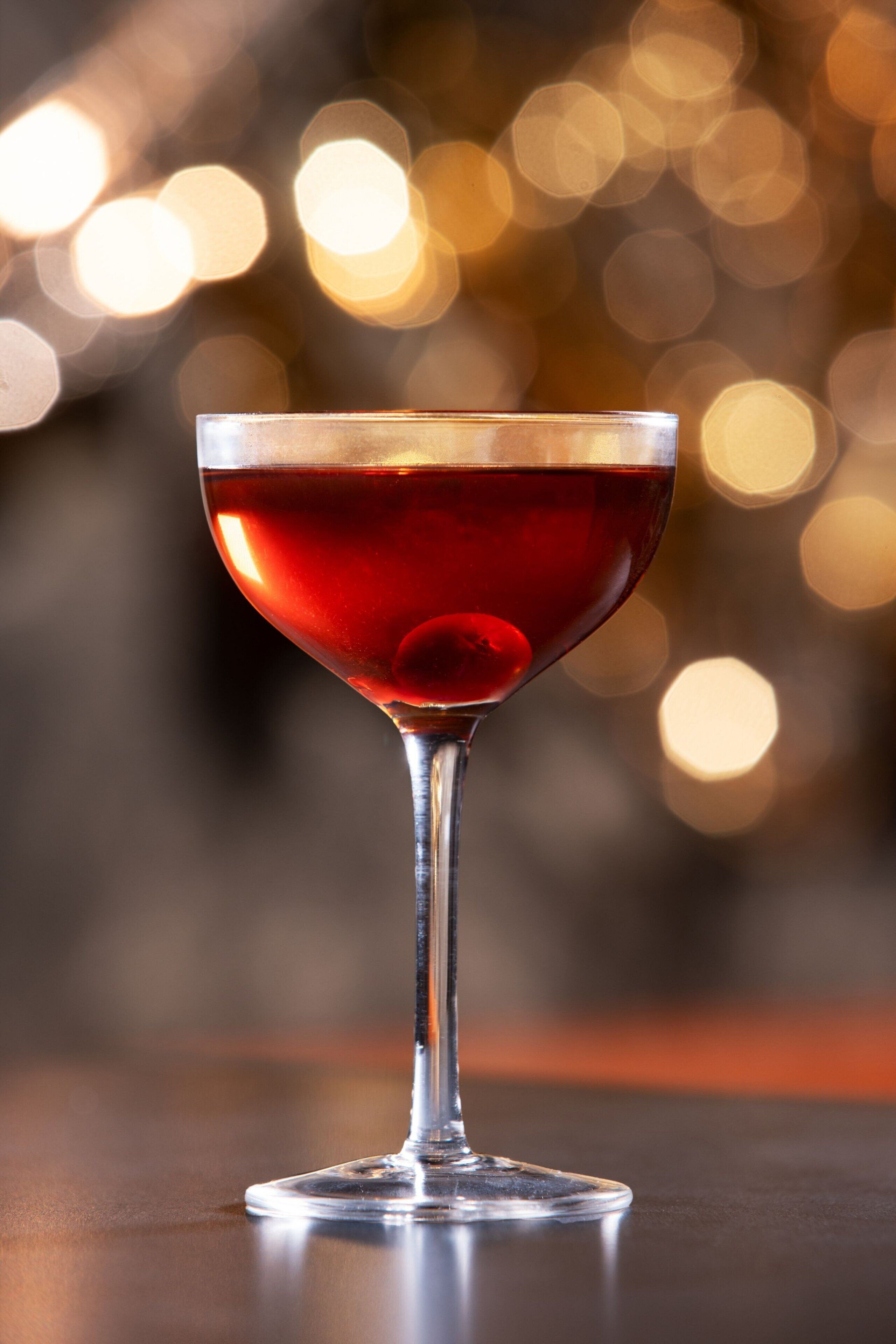 A martini glass with a red liquid on a reflective surface.