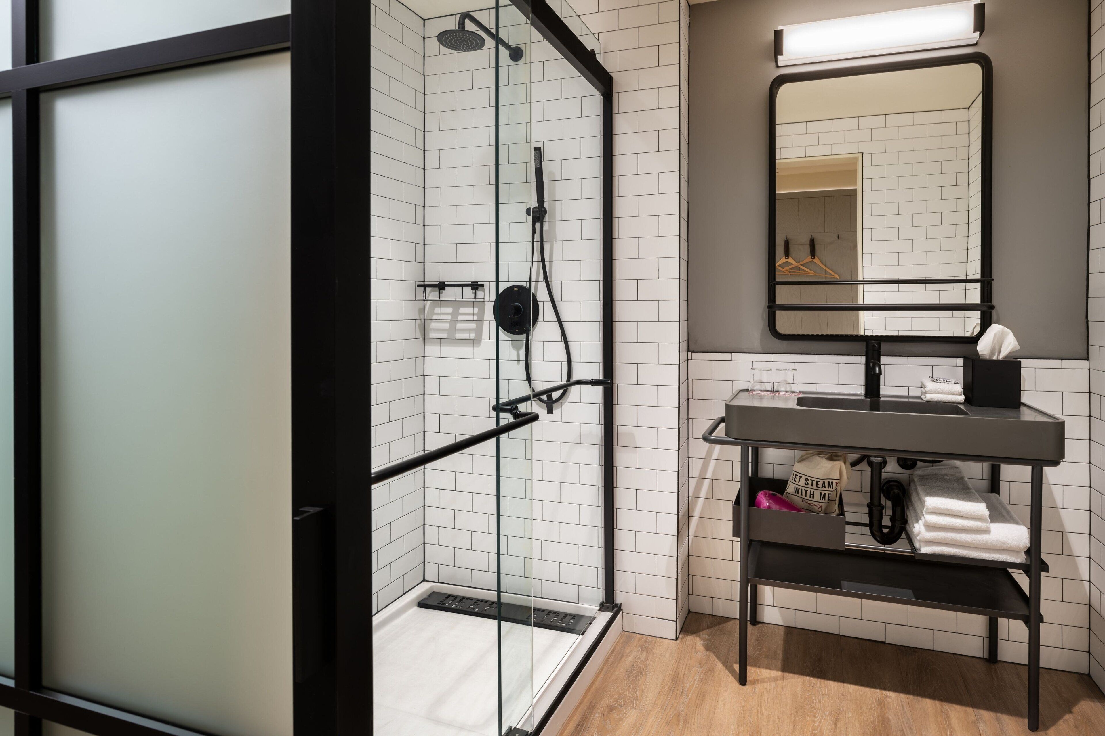 A modern bathroom with a glass-enclosed shower, a black-framed mirror, and a wooden floor.