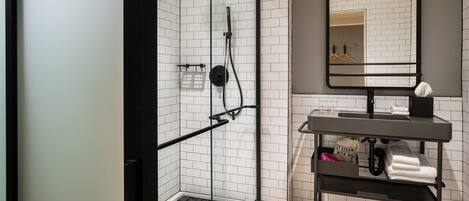 A modern bathroom with a glass-enclosed shower, a black-framed mirror, and a wooden floor.