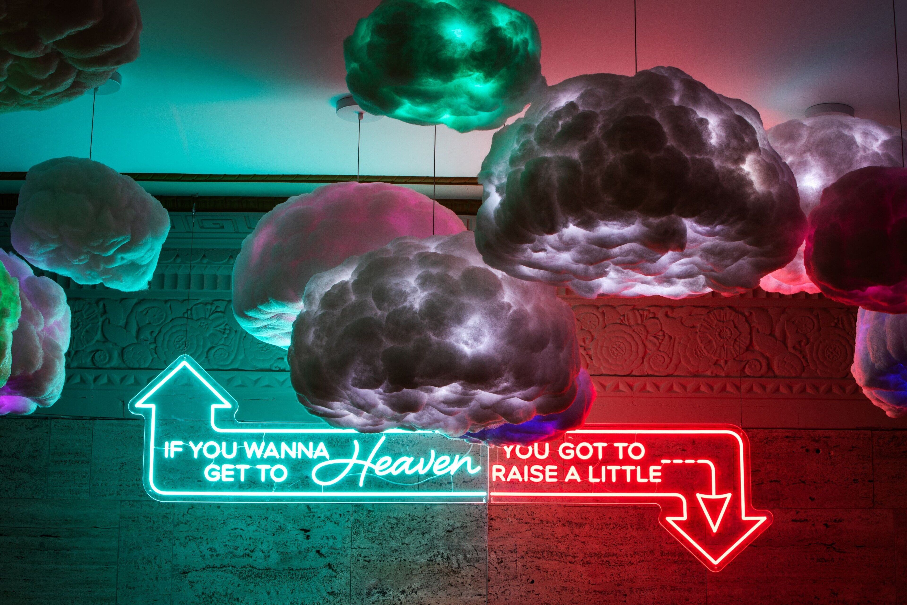A neon sign with a humorous message, surrounded by colorful cloud-like decorations.