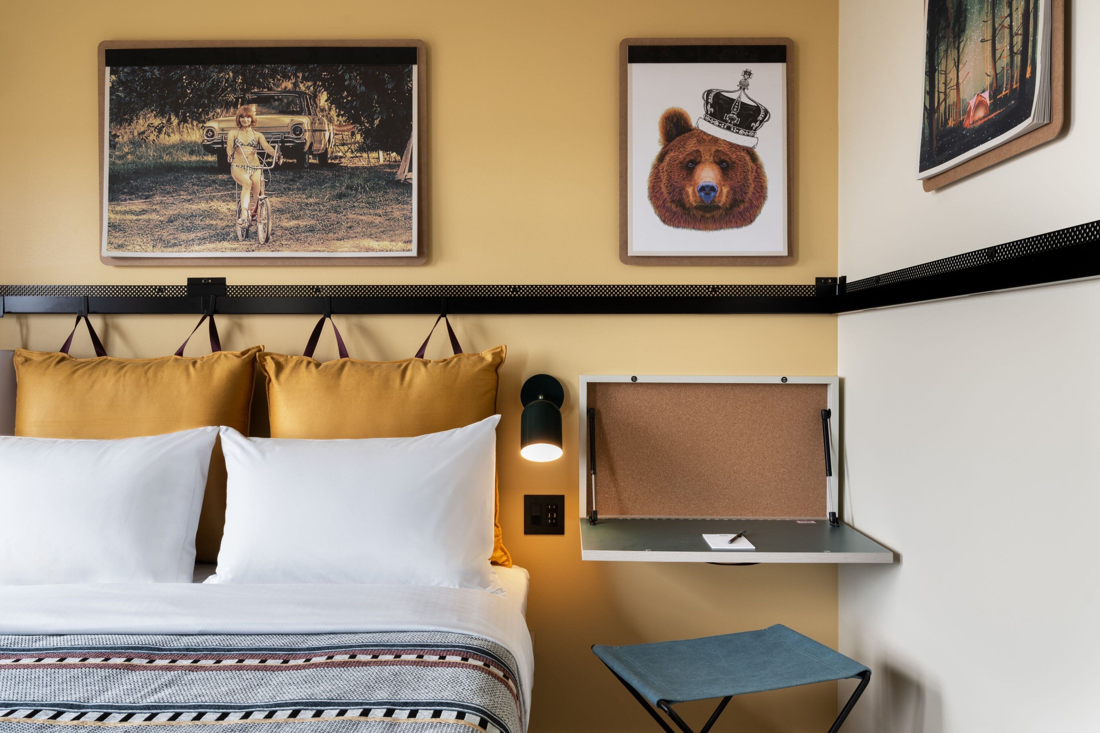A hotel room with a bed, a small table, a chair, and wall-mounted artwork.