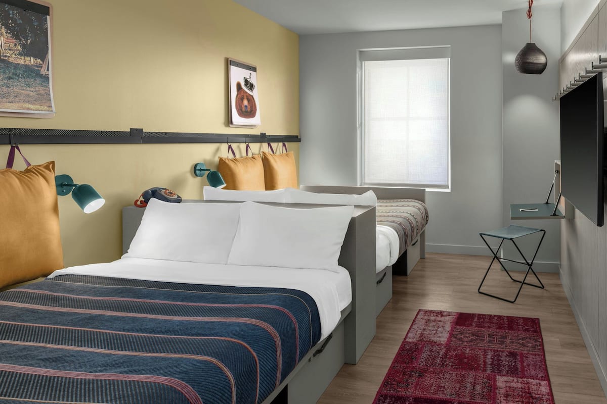 A modern bedroom with a large bed, a small table, a TV, and a window.