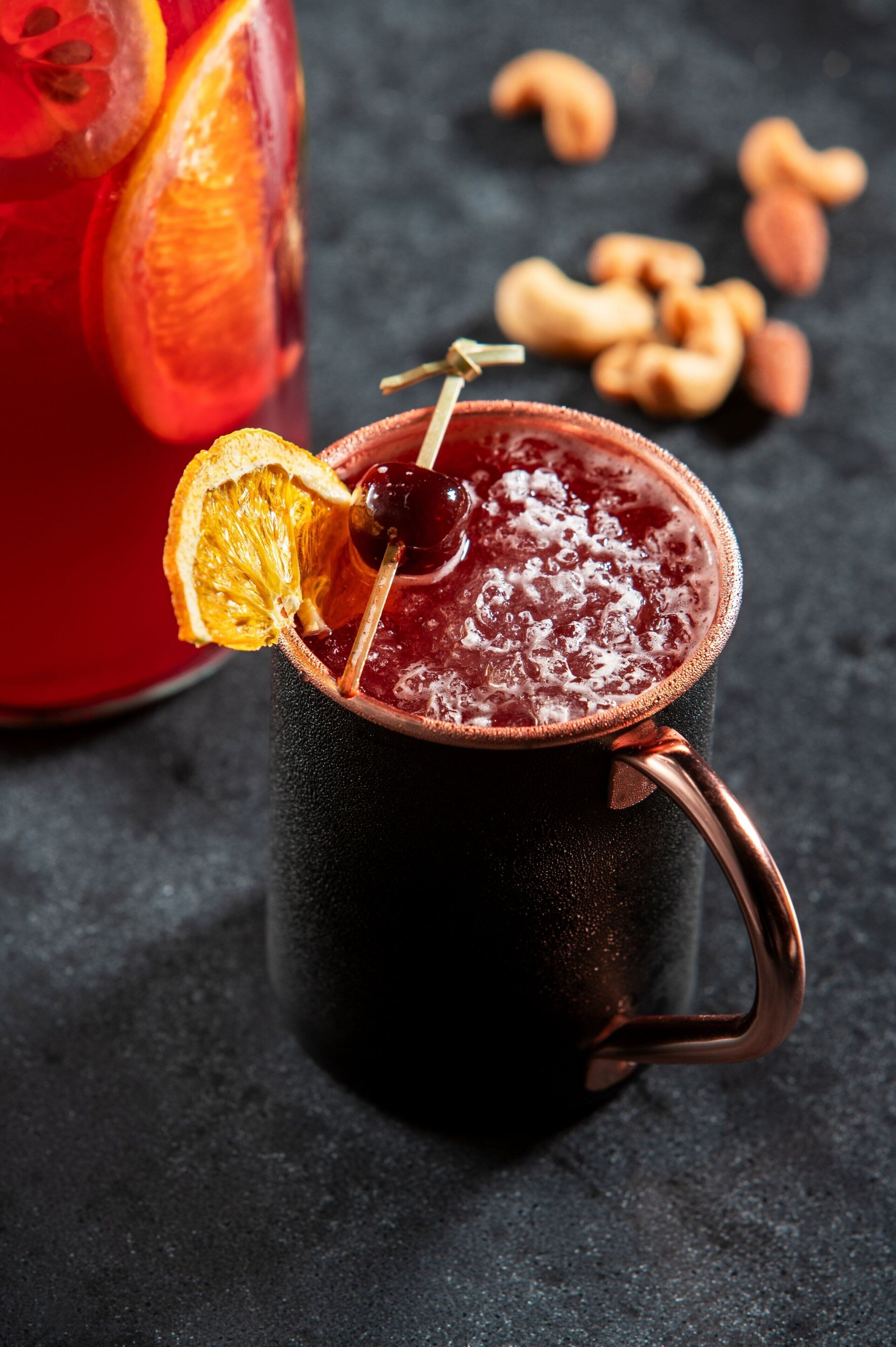 A dark mug with a straw and a dried orange slice on top, placed on a textured surface.