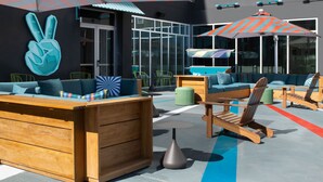 An outdoor seating area with wooden furniture, colorful cushions, and umbrellas. - Aloft by Marriott McAllen (McAllen)